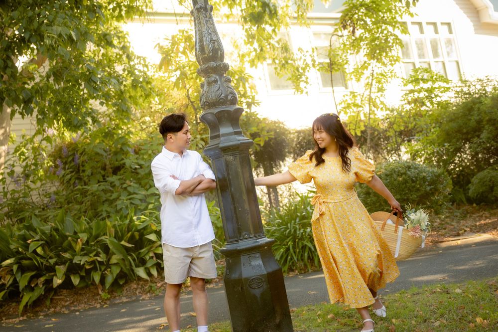 A couple in summer attire playfully interacts near a vintage lamp post in a park.