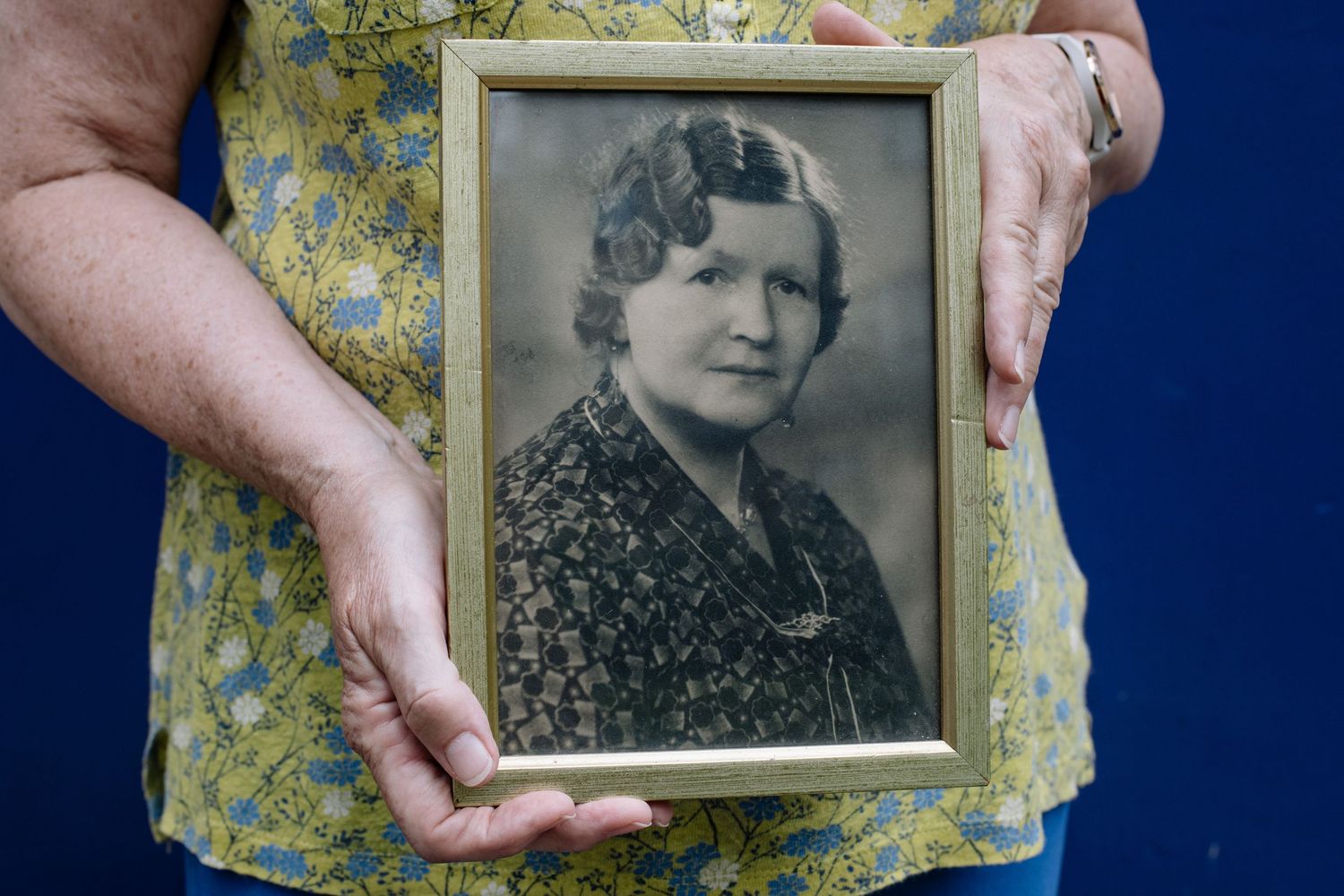 Hands holding vintage black and white portrait photographs against a dark blue background with yellow floral pattern.