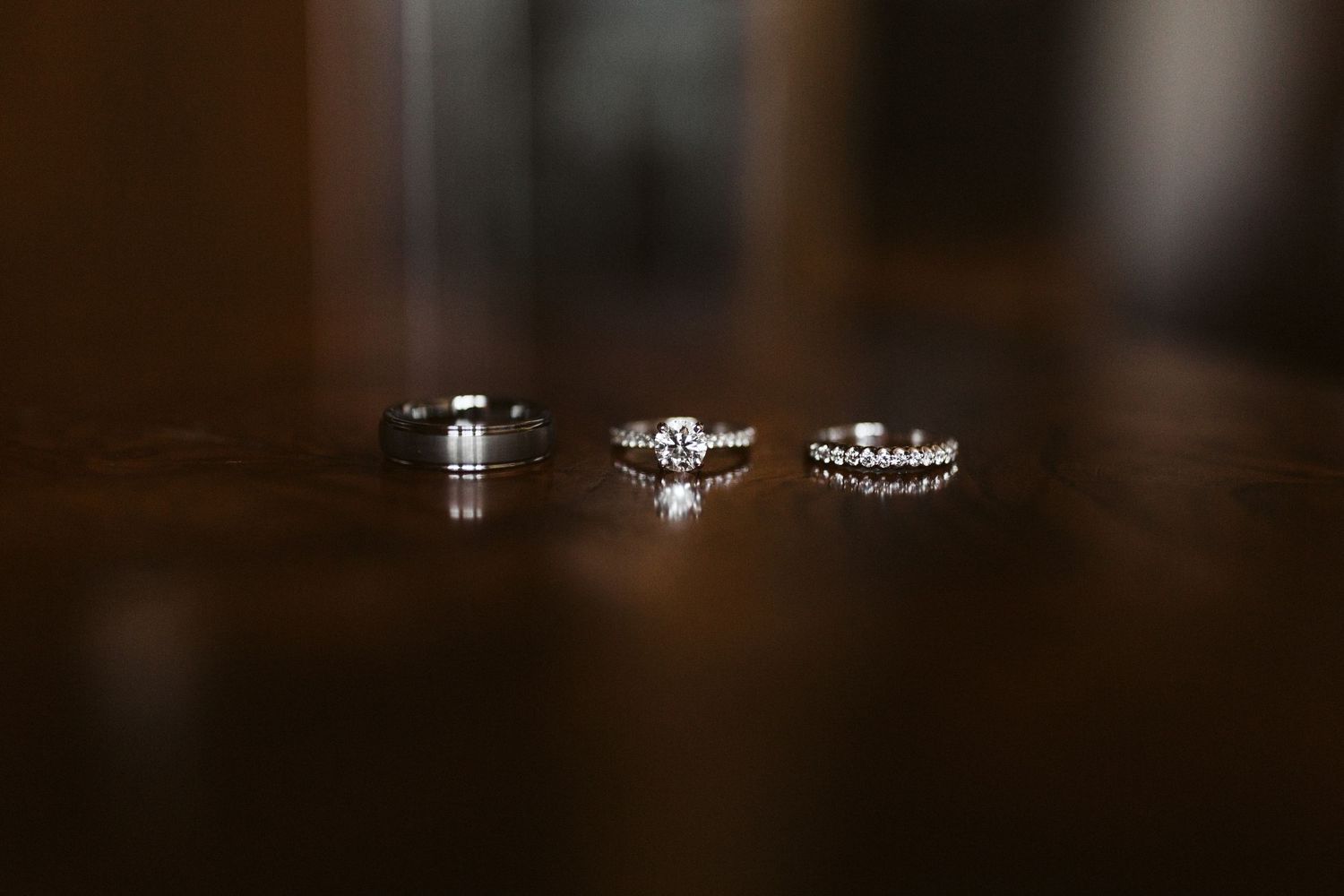Three diamond engagement rings and wedding bands displayed on a dark reflective surface with soft lighting.