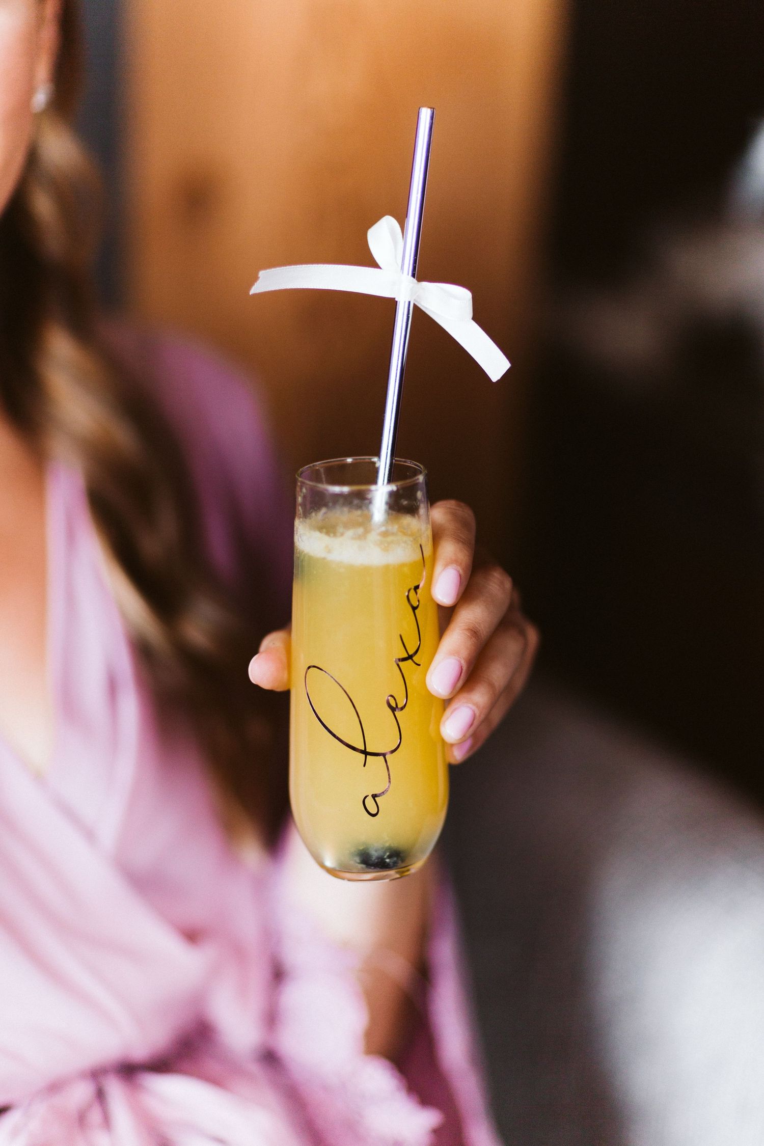 Three glasses of yellow cocktails with straws shown in sequence being sipped from a pink surface.