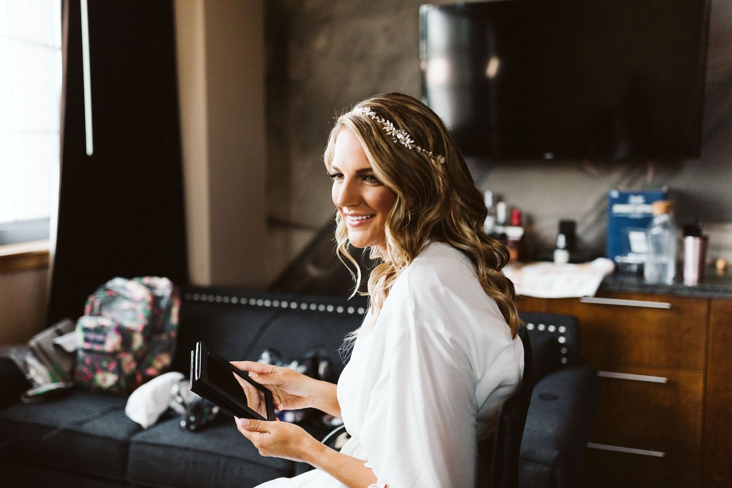 Bride in white robe checking phone during wedding preparations.