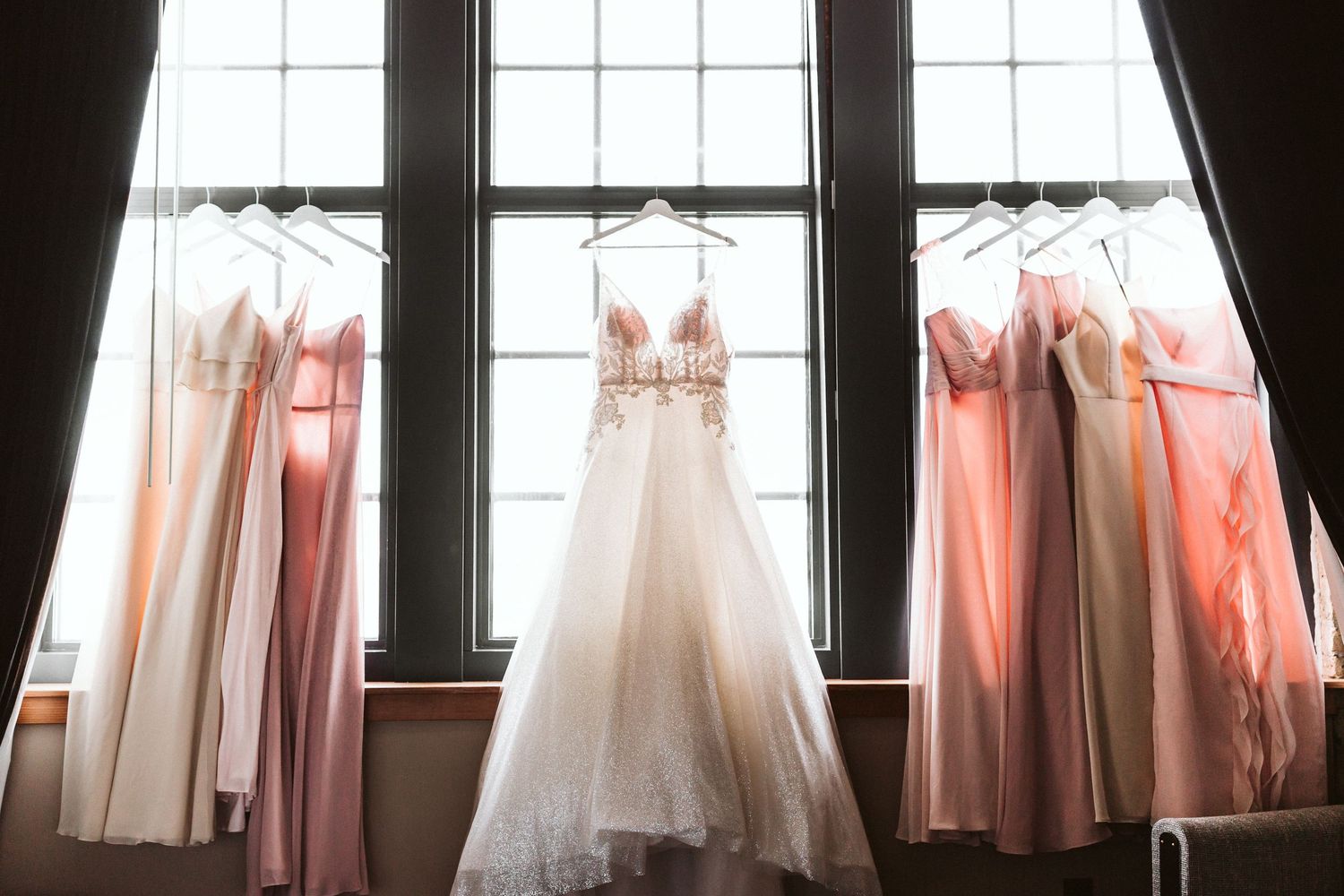 Pink and white tulle dresses hang in a row on display against a bright window creating an ethereal bridal boutique scene.