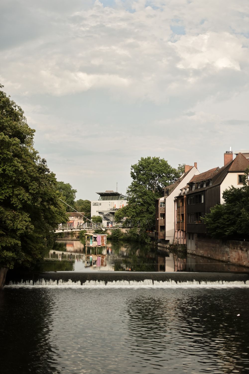 Scenic waterfront view of historic buildings and a small dam along a tranquil canal in a European town.