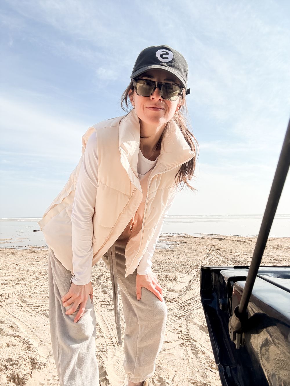 Person in light colored clothing and baseball cap leans against small aircraft on sunny desert terrain.
