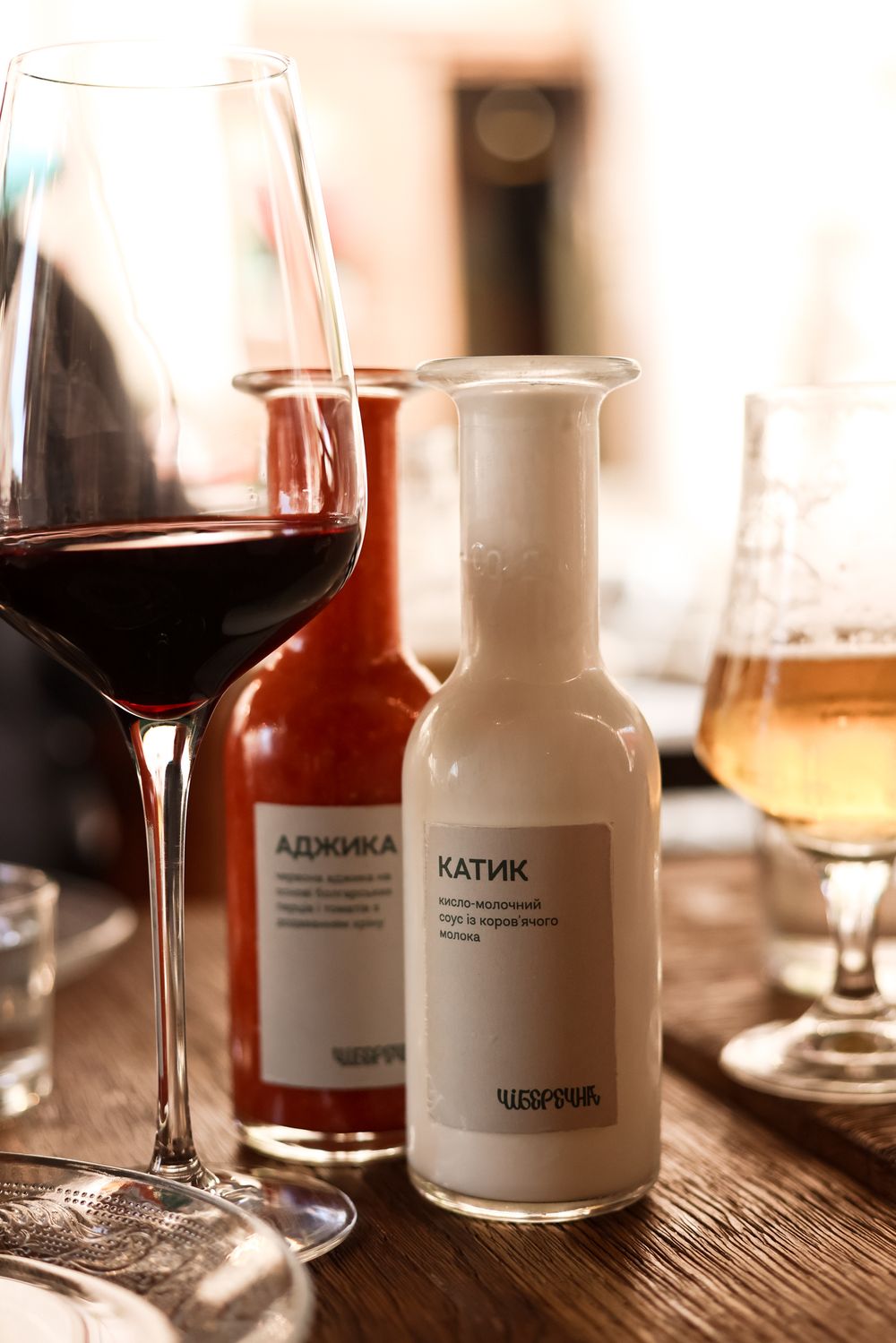 Wine glasses and white bottles with labels sit on a rustic wooden table in warm lighting.