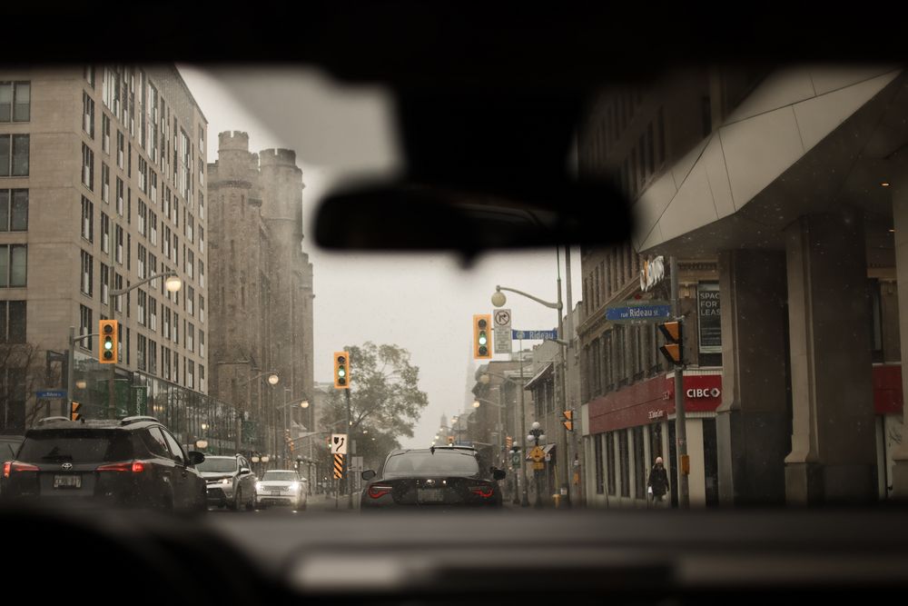 Foggy city street view with tall buildings and traffic lights casting an eerie glow through the mist.