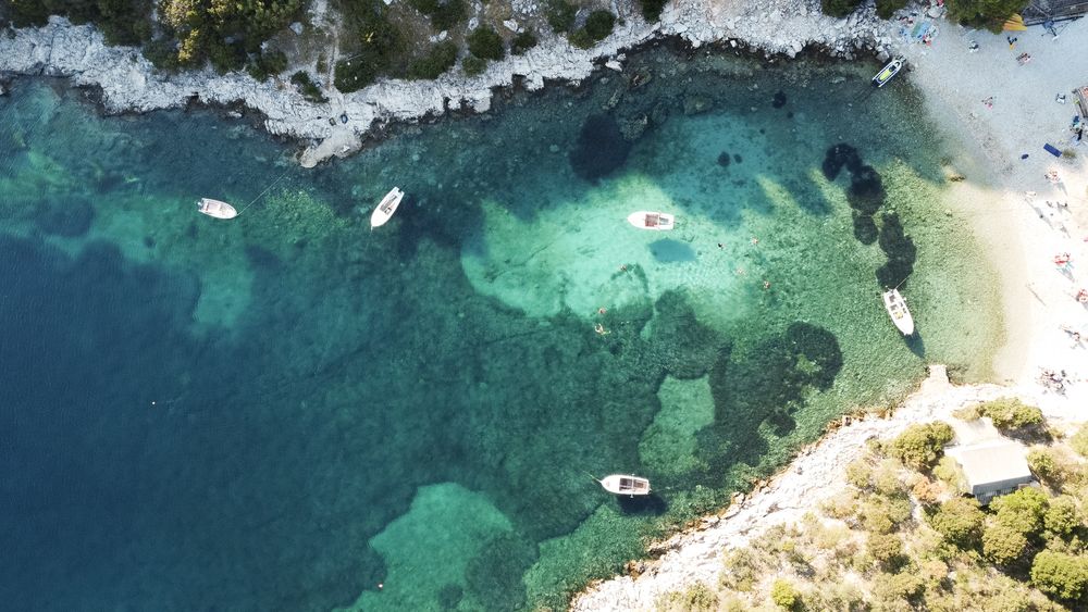 Aerial view of turquoise Mediterranean waters with boats anchored near rocky coastline and sandy beaches.