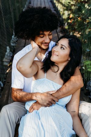A happy couple embracing on a wooden bridge, the woman in a blue striped dress leaning into her partners arms.