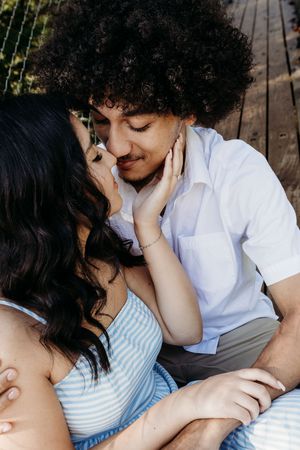 A couple sharing an intimate moment, the woman gently holding the mans face as they lean in for a kiss outdoors.