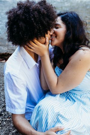 A joyful couple sharing a kiss near a waterfall, the woman in a blue striped dress smiling as they embrace.