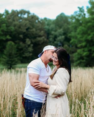 Happy engaged couple embracing and laughing together in a golden wheat field with forest background.