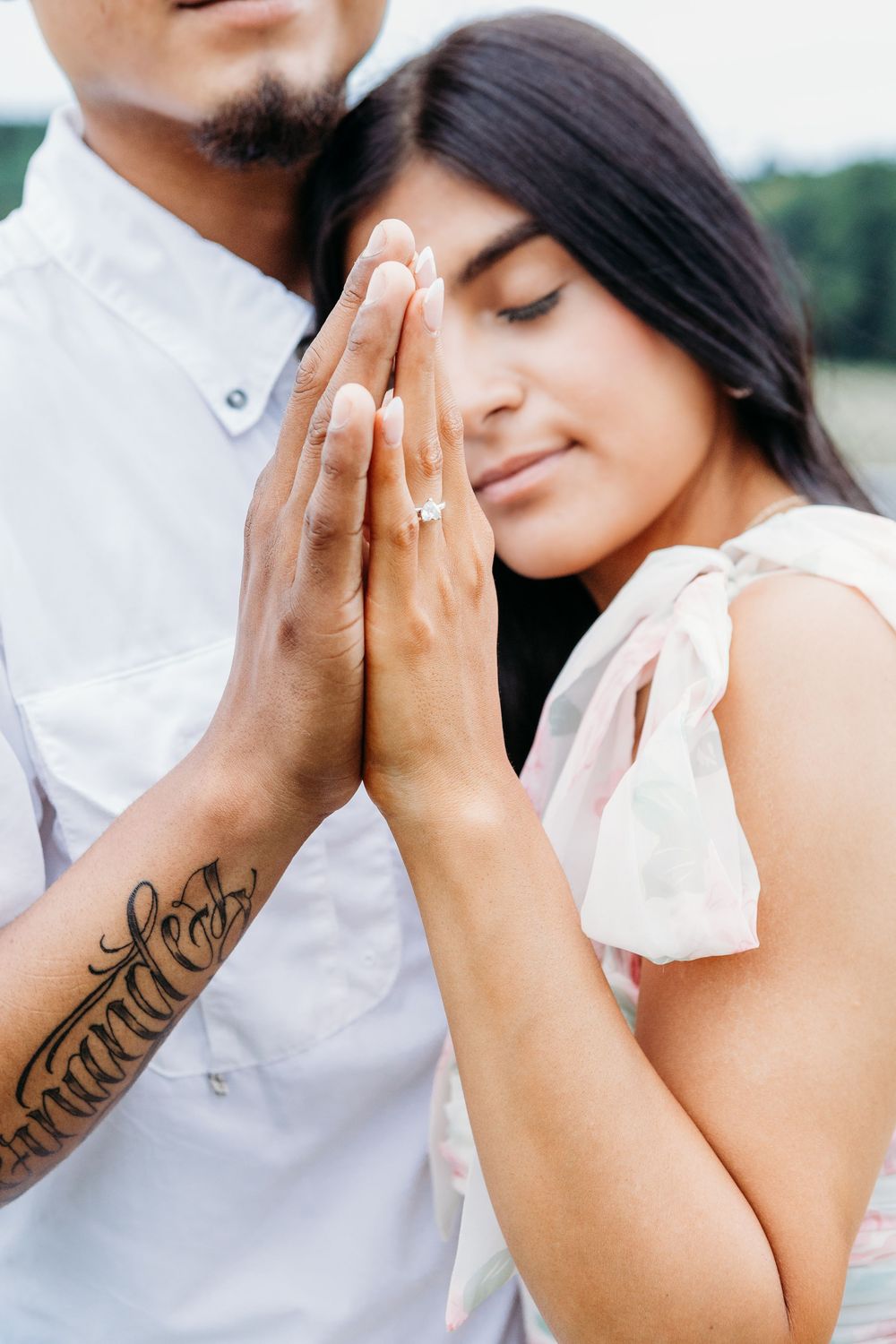 Close-up of engaged couple holding hands, showcasing diamond engagement ring and arm tattoo.