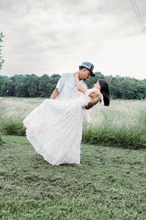 Couple shares a romantic dip and kiss in a lush green field during outdoor engagement session.