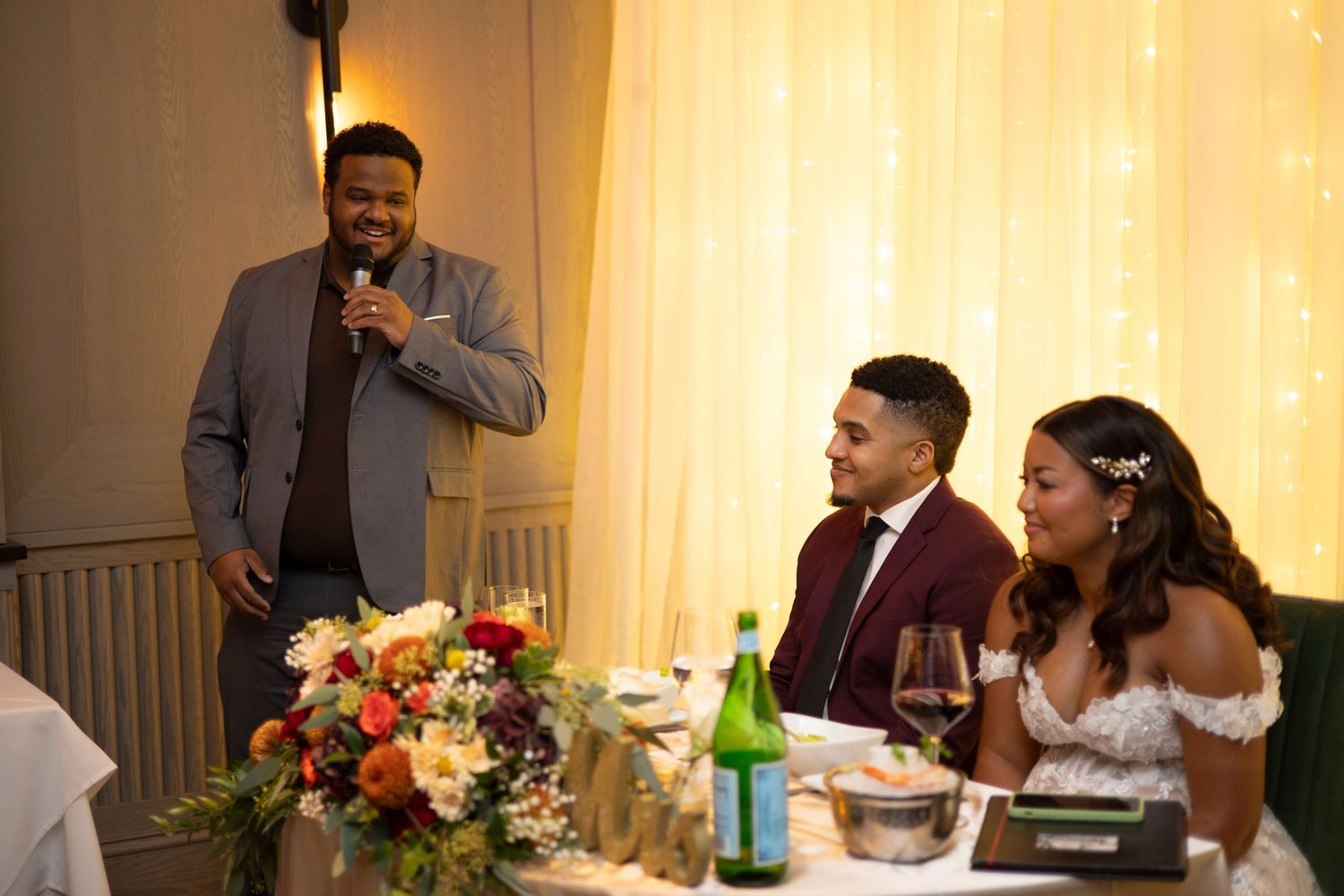 Wedding guests laugh and socialize at elegant reception tables decorated with colorful floral centerpieces.