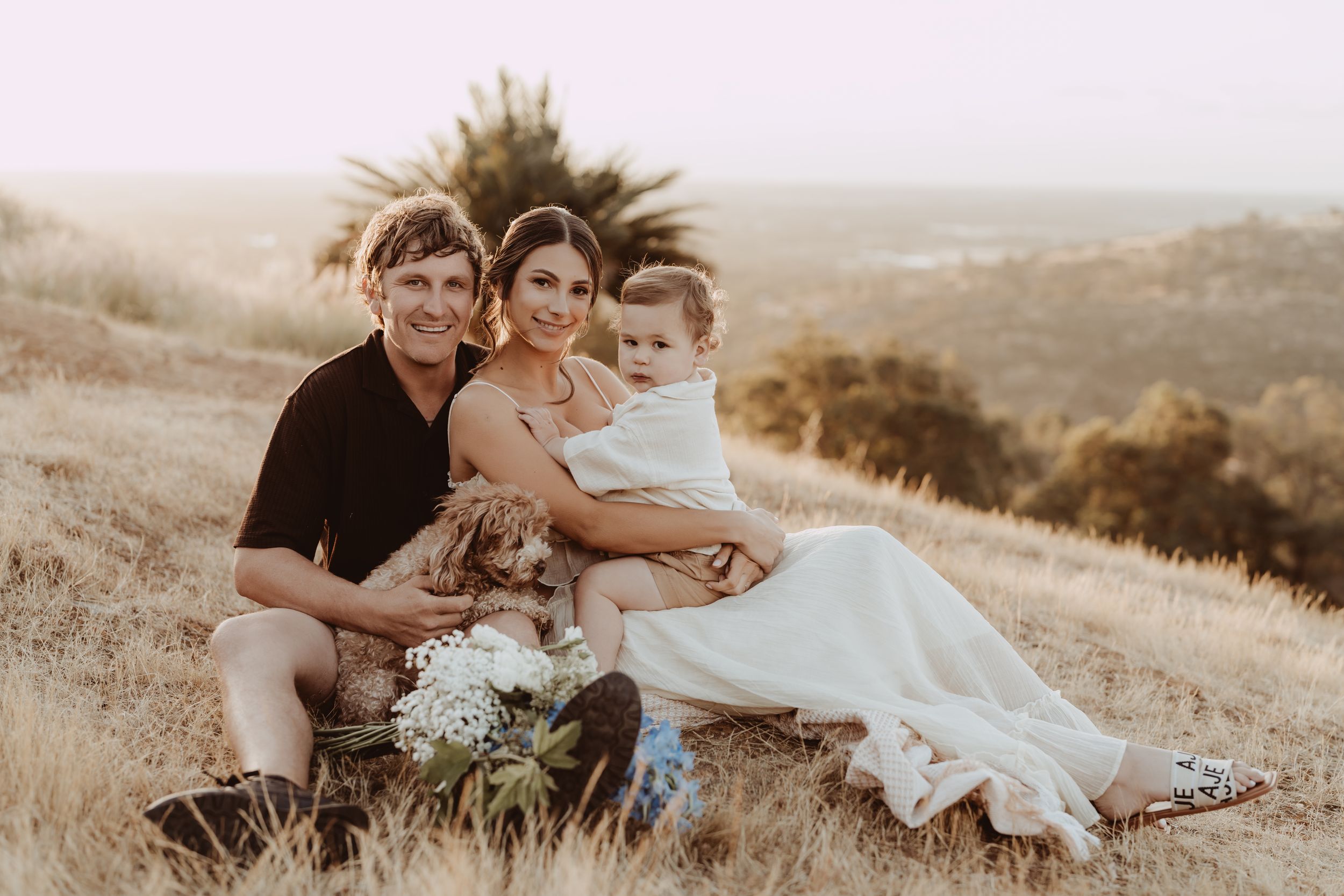 A couple in wedding attire embraces on a sunlit hilltop during golden hour.