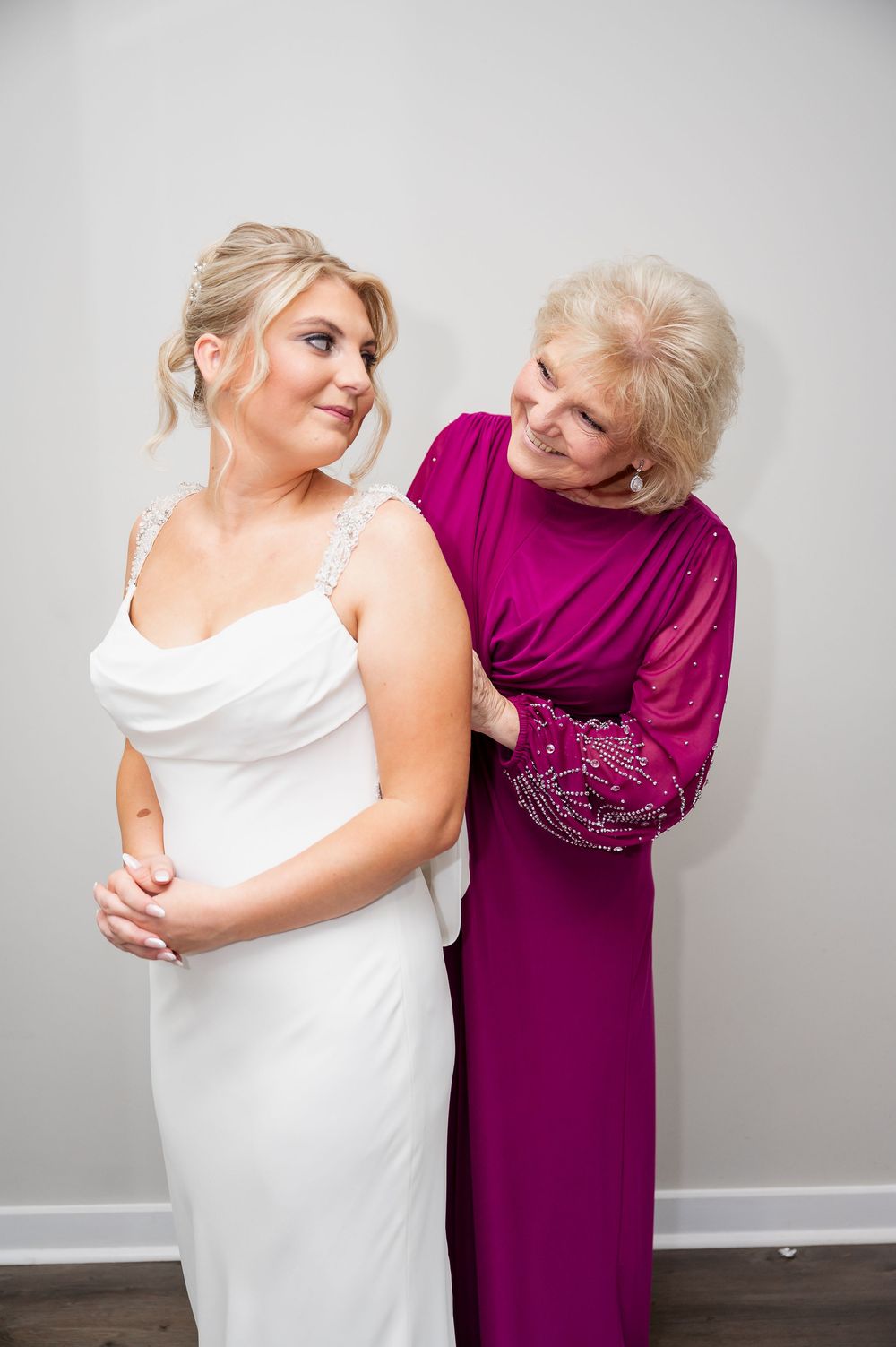 Emotional moment between bride in white dress and woman in purple during wedding preparations.