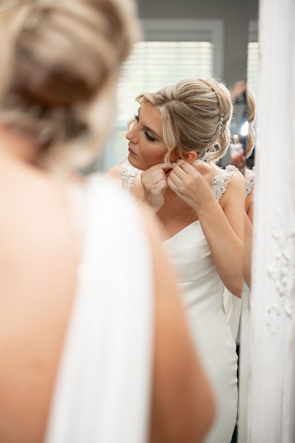 Bride putting on earrings while looking in mirror during wedding preparations.