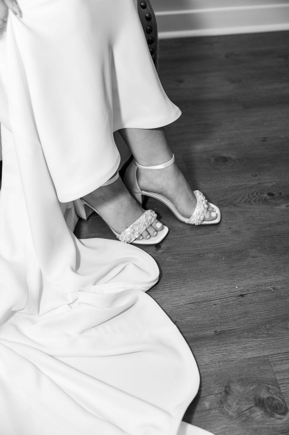 Detail shot of white wedding dress and bridal shoes on dark wooden flooring.