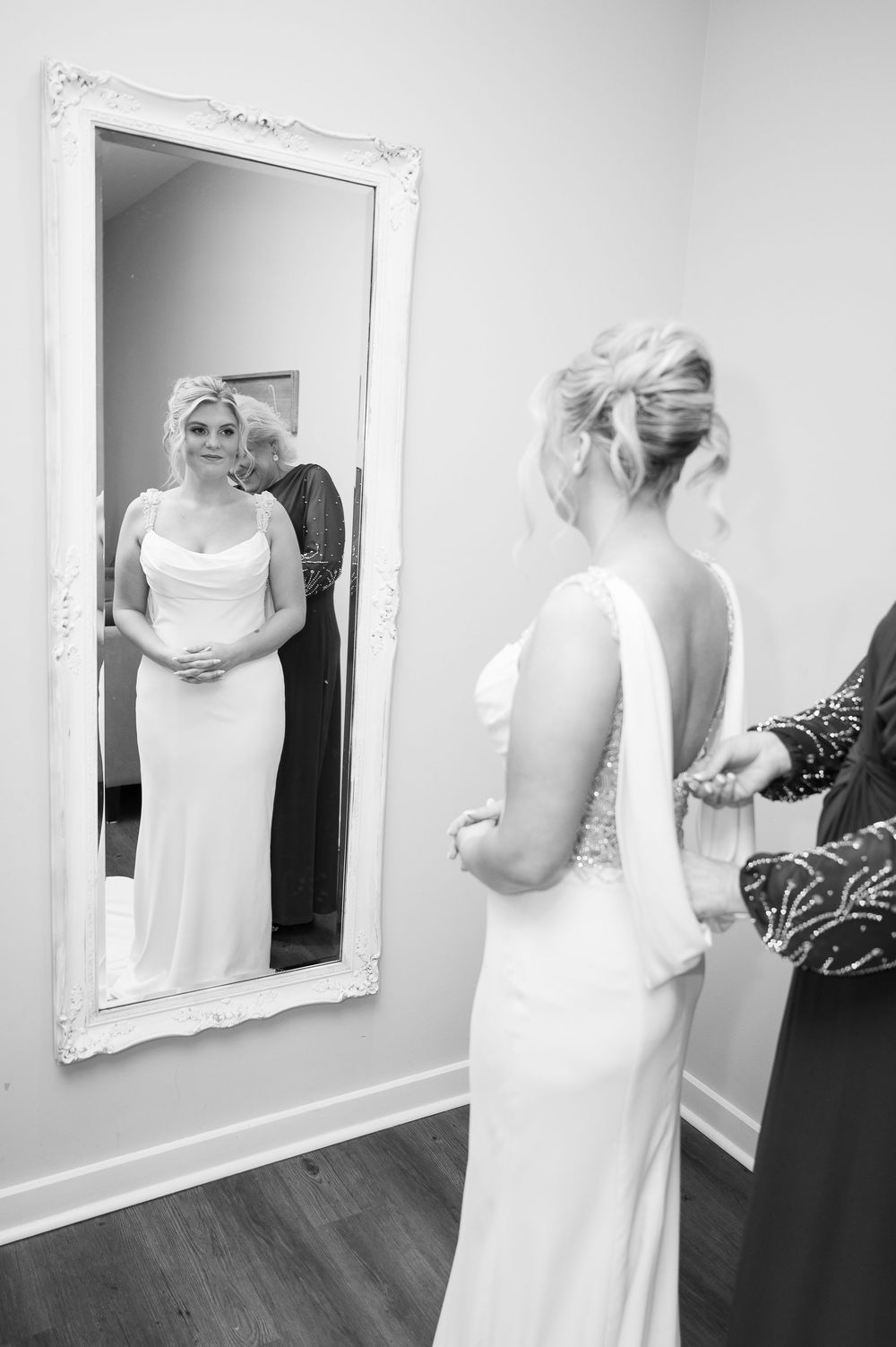 Bride getting ready in white dress looking at ornate mirror reflections.