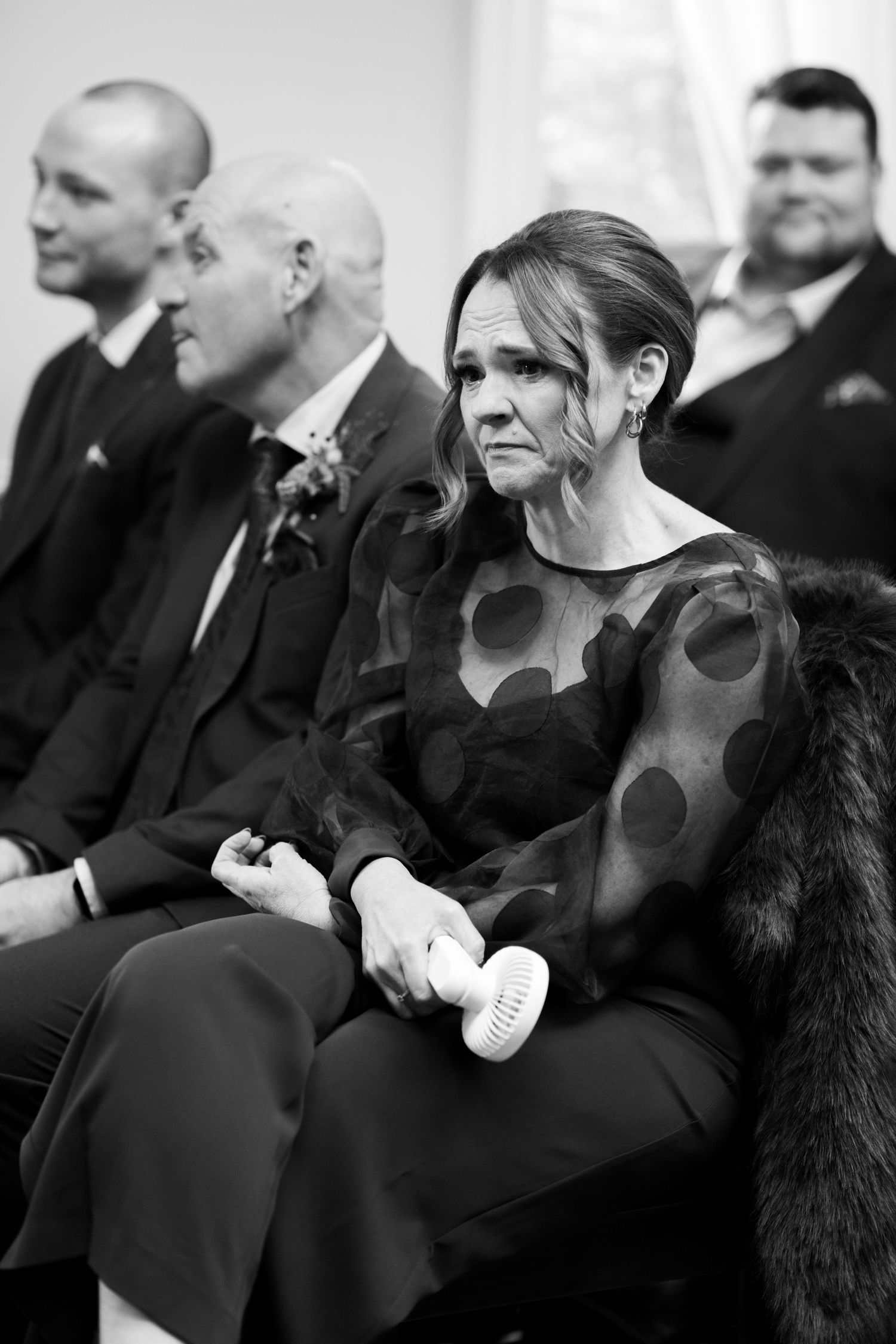 A row of people dressed in black formal attire sit together at an event or ceremony.