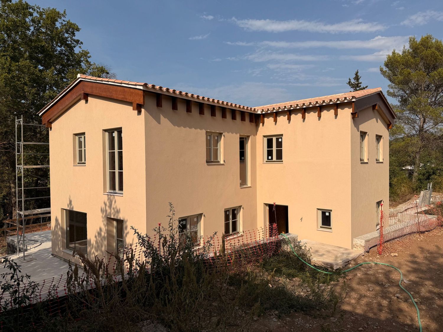 Panoramic view of a Mediterranean-style beige stucco house with terracotta roof tiles and multiple windows.
