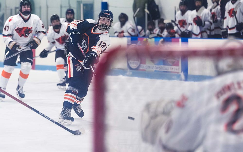 Trojans player takes a shot on goal with the puck in front of the net by SportsFox Photography, Hershey PA.