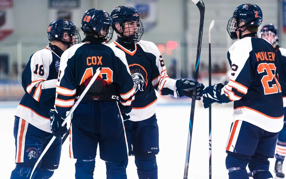 Trojans players huddle together on the ice, sticks raised after a big play by SportsFox Photography, Hershey PA.
