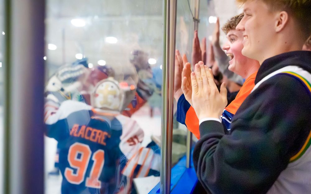 Trojans fan cheers and presses hands to the glass celebrating with players by SportsFox Photography, Hershey PA.