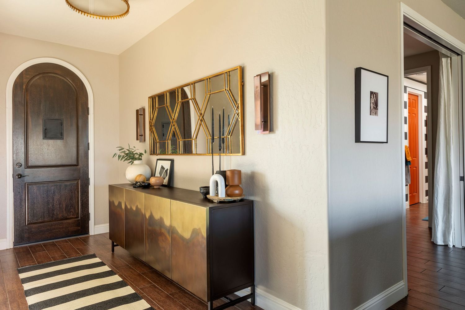 Modern entryway with arched doorway, striped rug, dark wood credenza and abstract wall art in neutral tones.