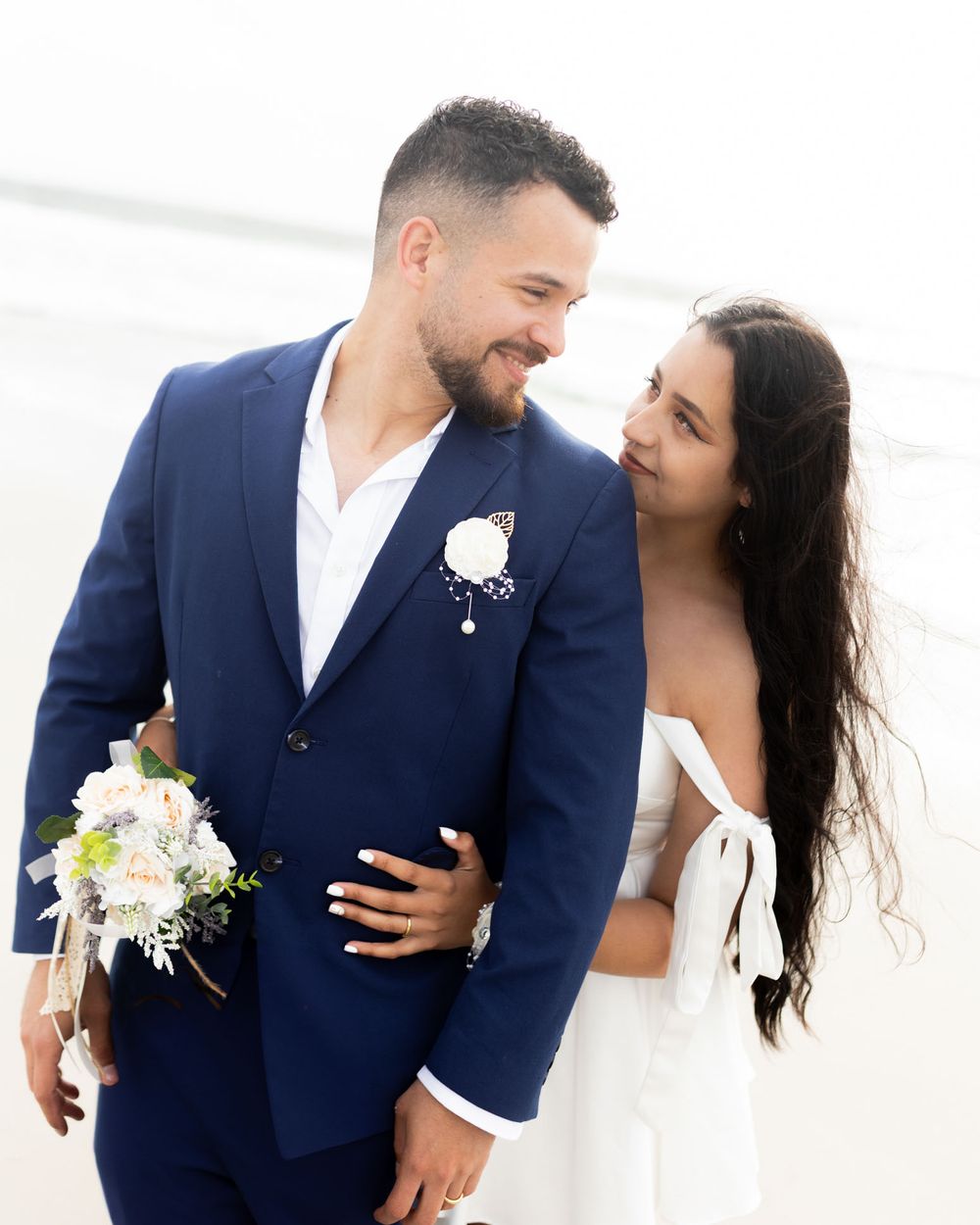 Wedding couple in navy and white embracing on beach in romantic photo sequence.