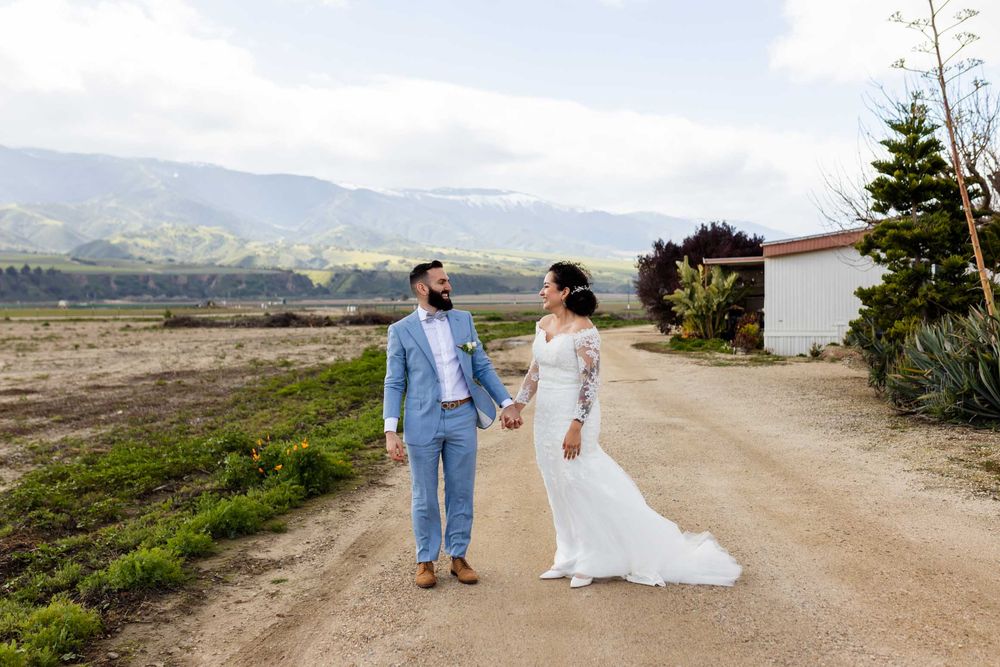 Wedding couple walks hand in hand on a scenic mountain path with distant hills in view.