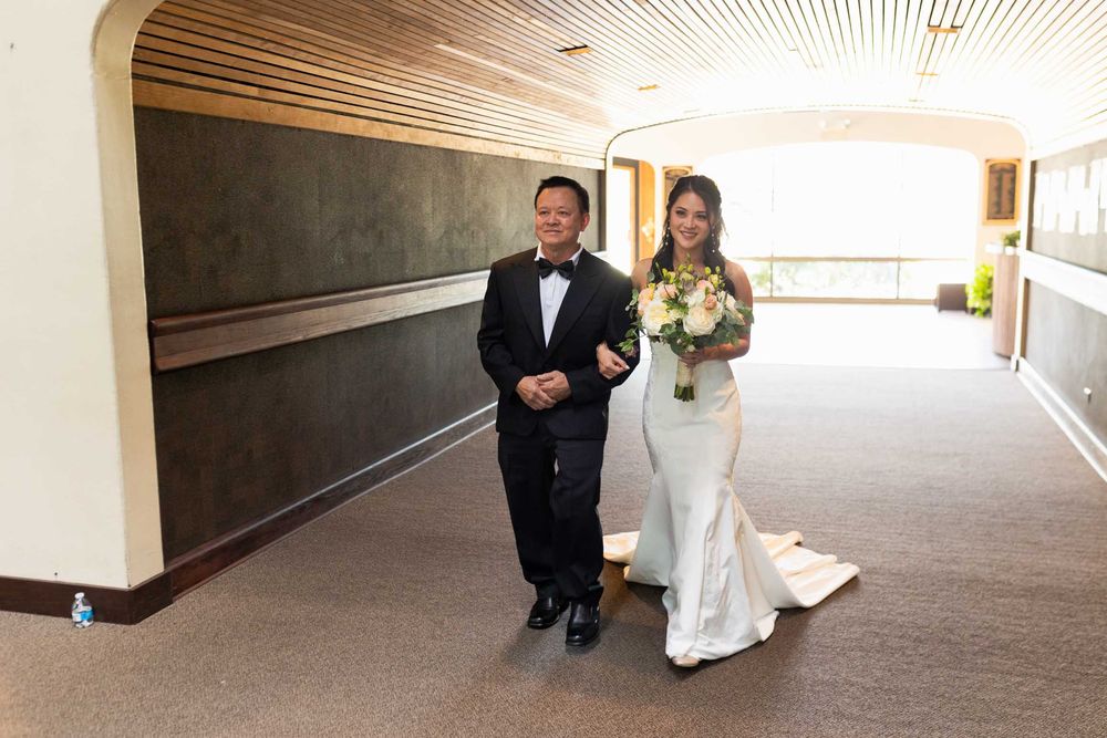 Couple walks down a modern hallway with wooden ceiling details during their wedding day celebration.