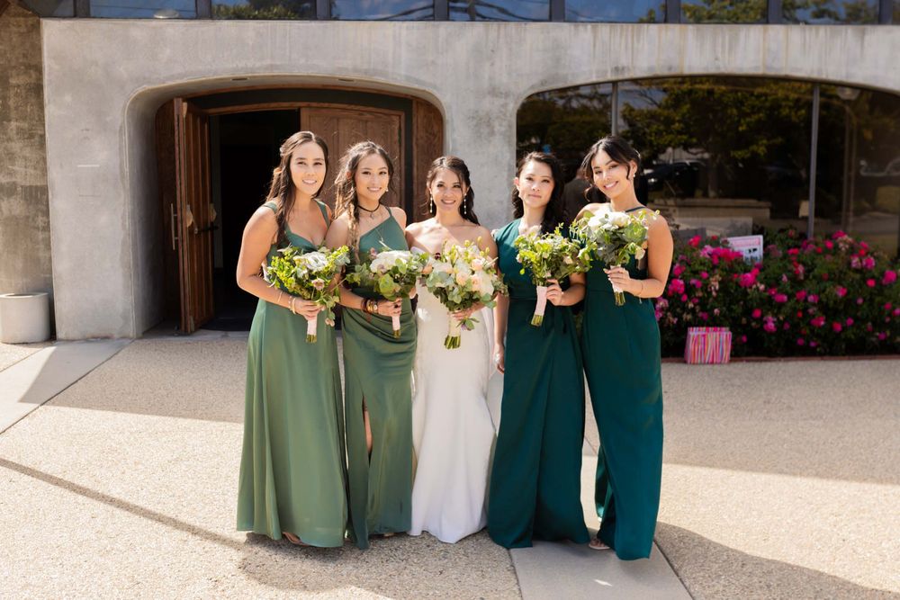 Wedding party in coordinated green dresses posing together outside a venue.