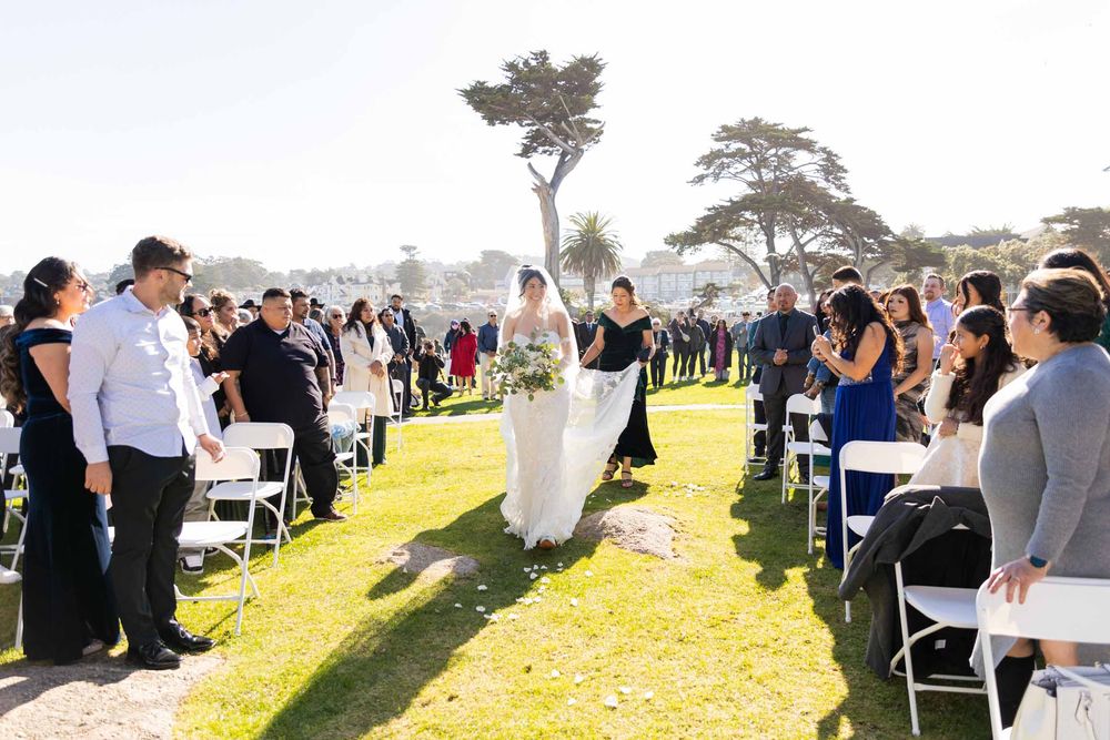 Outdoor wedding ceremony setup with white chairs on a grassy hillside overlooking the ocean.
