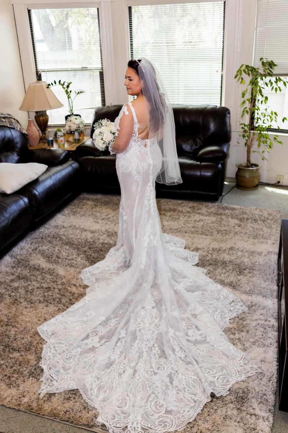 Stunning lace wedding dress with cathedral train displayed in a bright room with large windows.