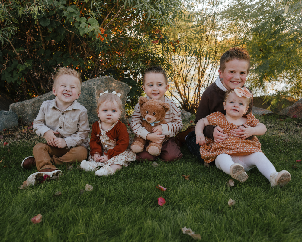 Five young children sitting together on green lawn in autumn garden.