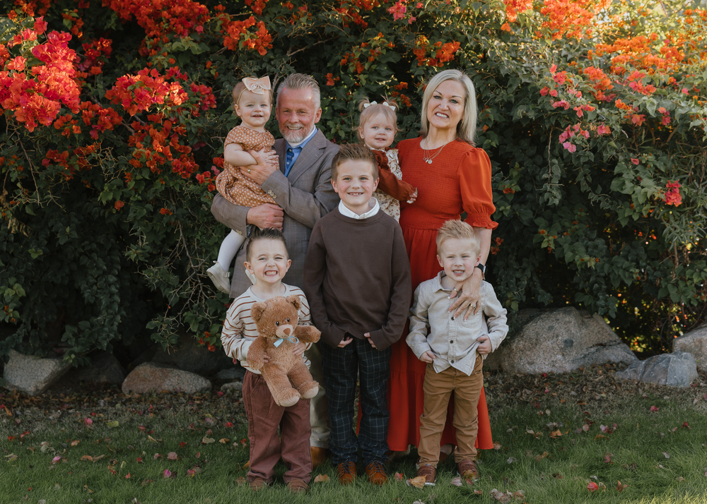 Family of seven posing with young children in front of red blooming shrub.