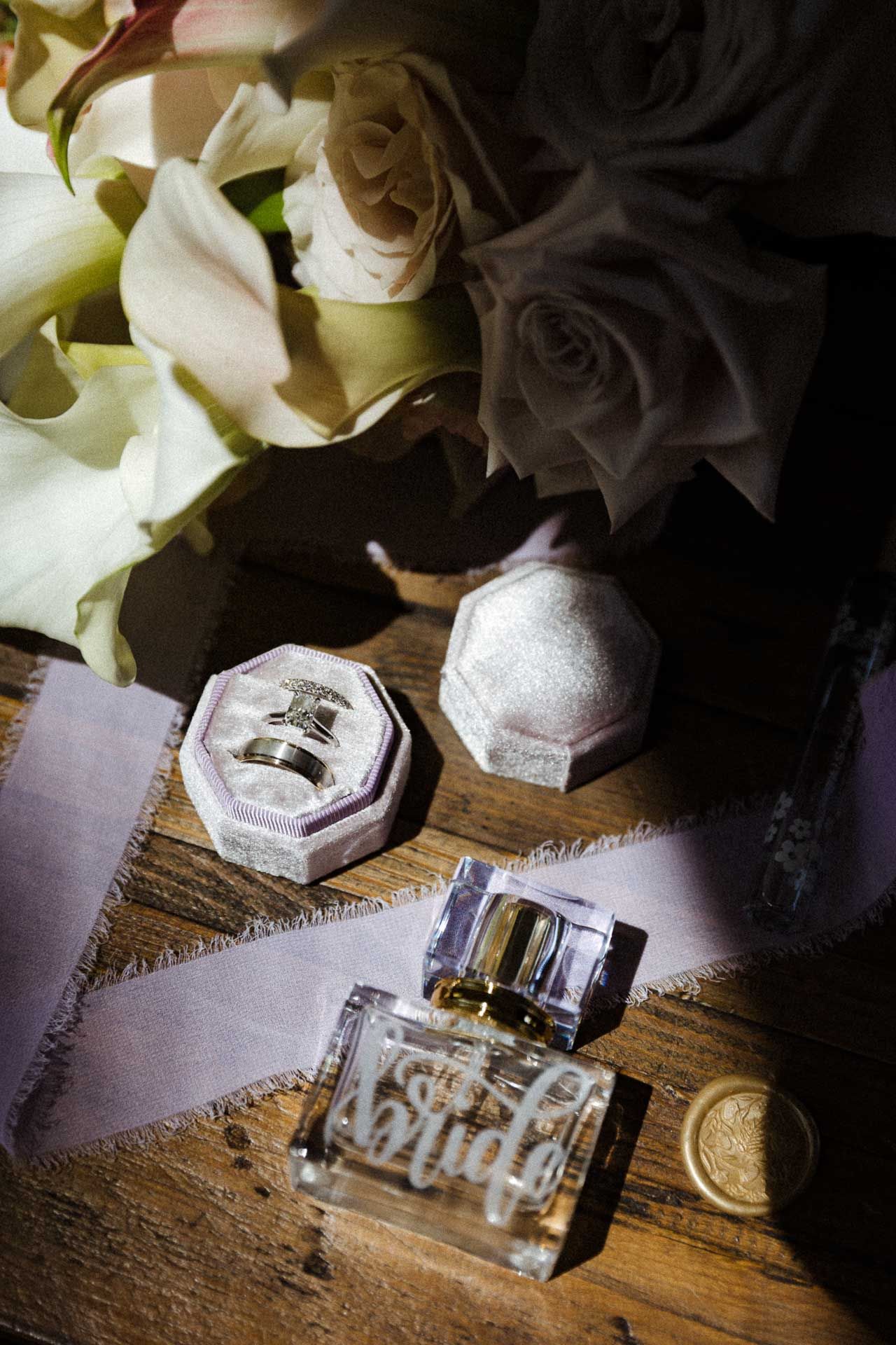 Perfume bottle and jewelry box arranged with white roses on rustic wooden surface in moody lighting.