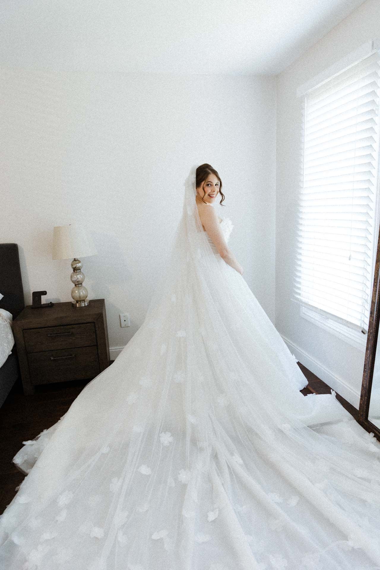 Dramatic full-length shots of a flowing white wedding gown with cathedral train in a bright room with windows.