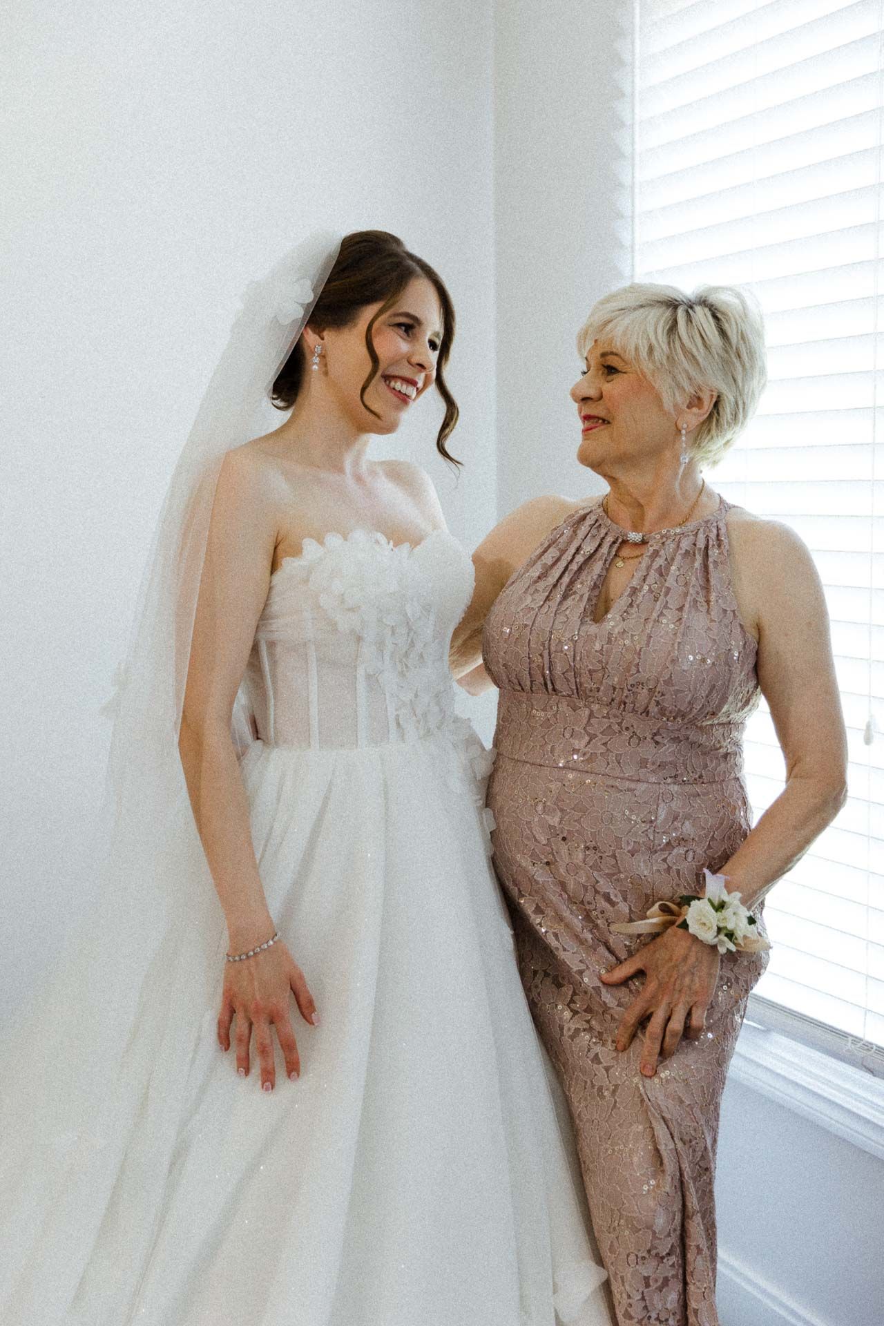Sweet candid moments between a bride in a white ballgown and an older woman in a mauve formal dress.