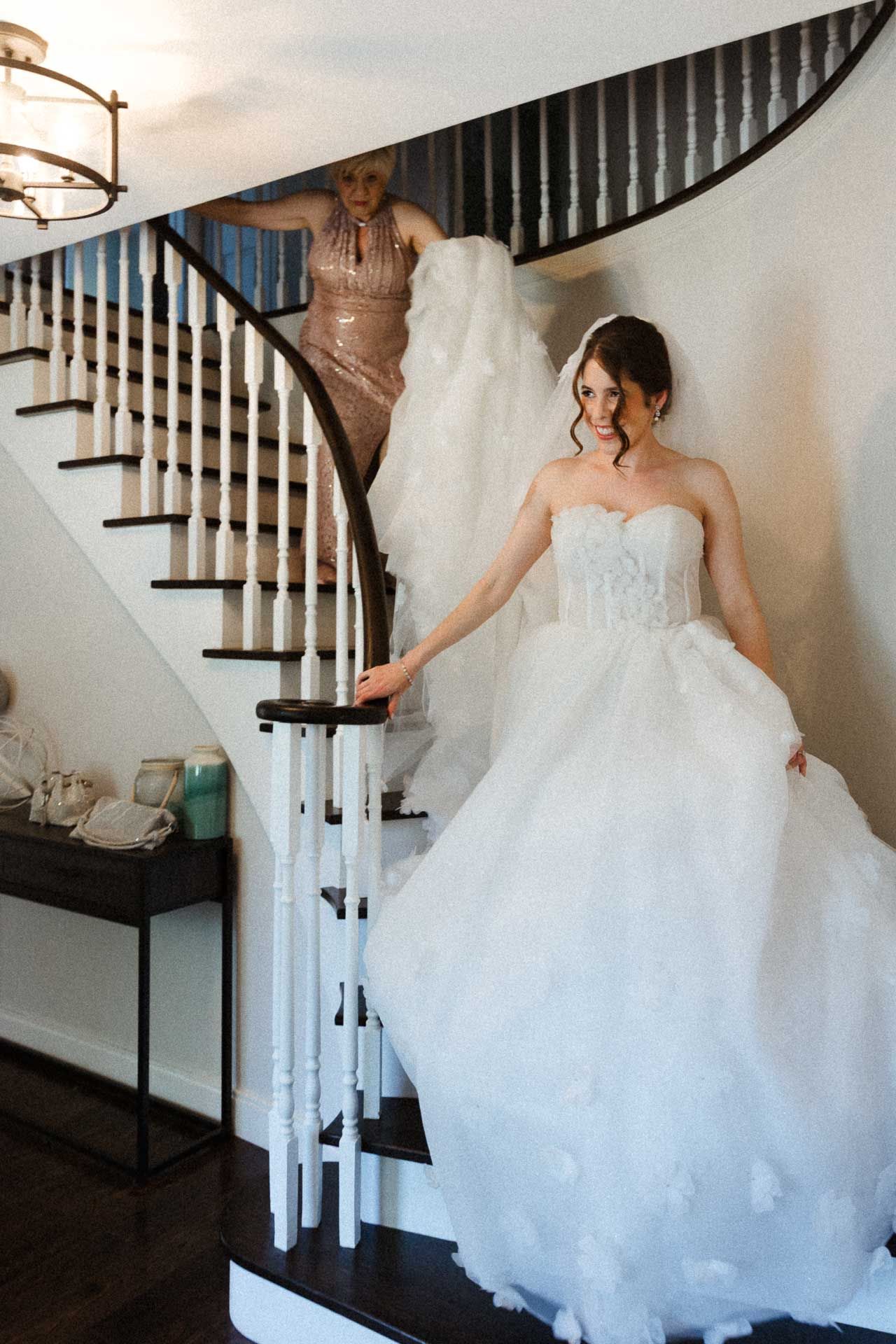 A bride in a flowing white strapless gown descends an elegant curved staircase.