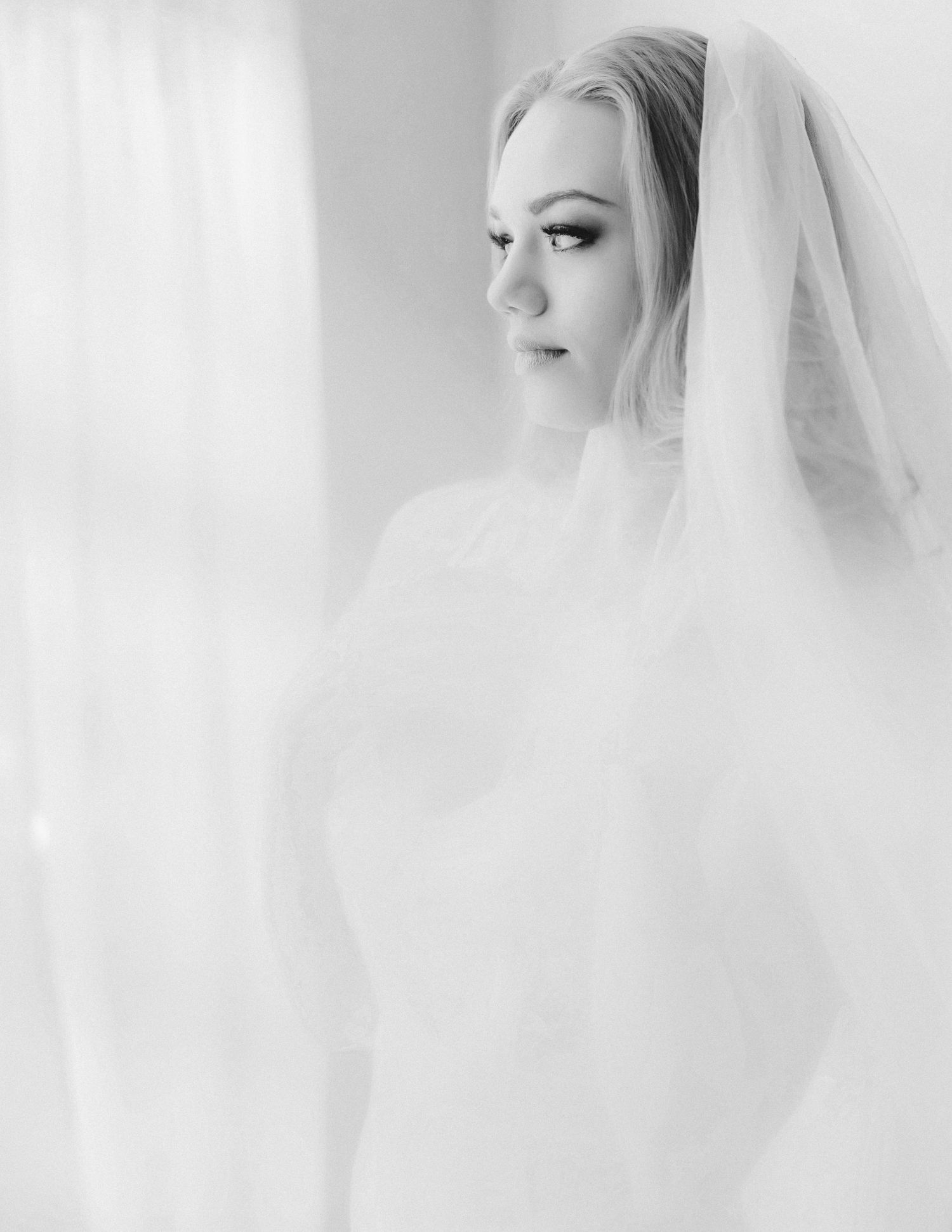 A bride in a white wedding dress and veil poses elegantly in a bright, ethereal setting. Columbus bridal boudoir
