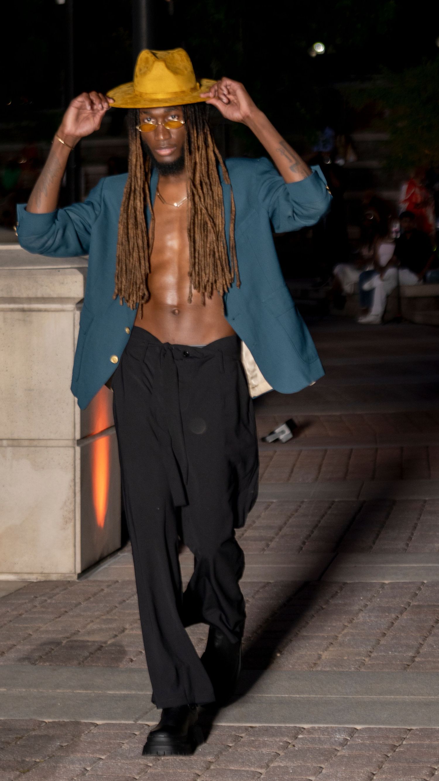A fashion model wearing a teal blazer and black pants strikes dynamic poses in an outdoor evening photoshoot.