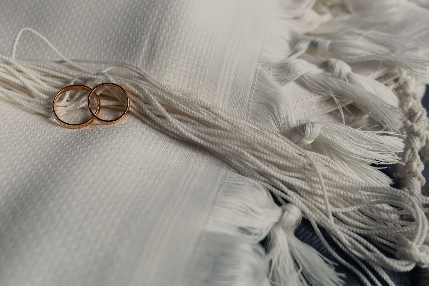 Two gold wedding rings rest on delicate white fringe fabric with soft textural details.