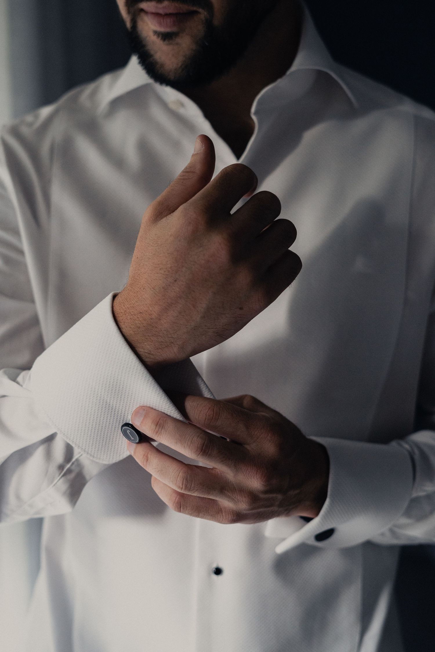 Close-up shots of hands adjusting white dress shirt cuffs and sleeves in dramatic lighting.