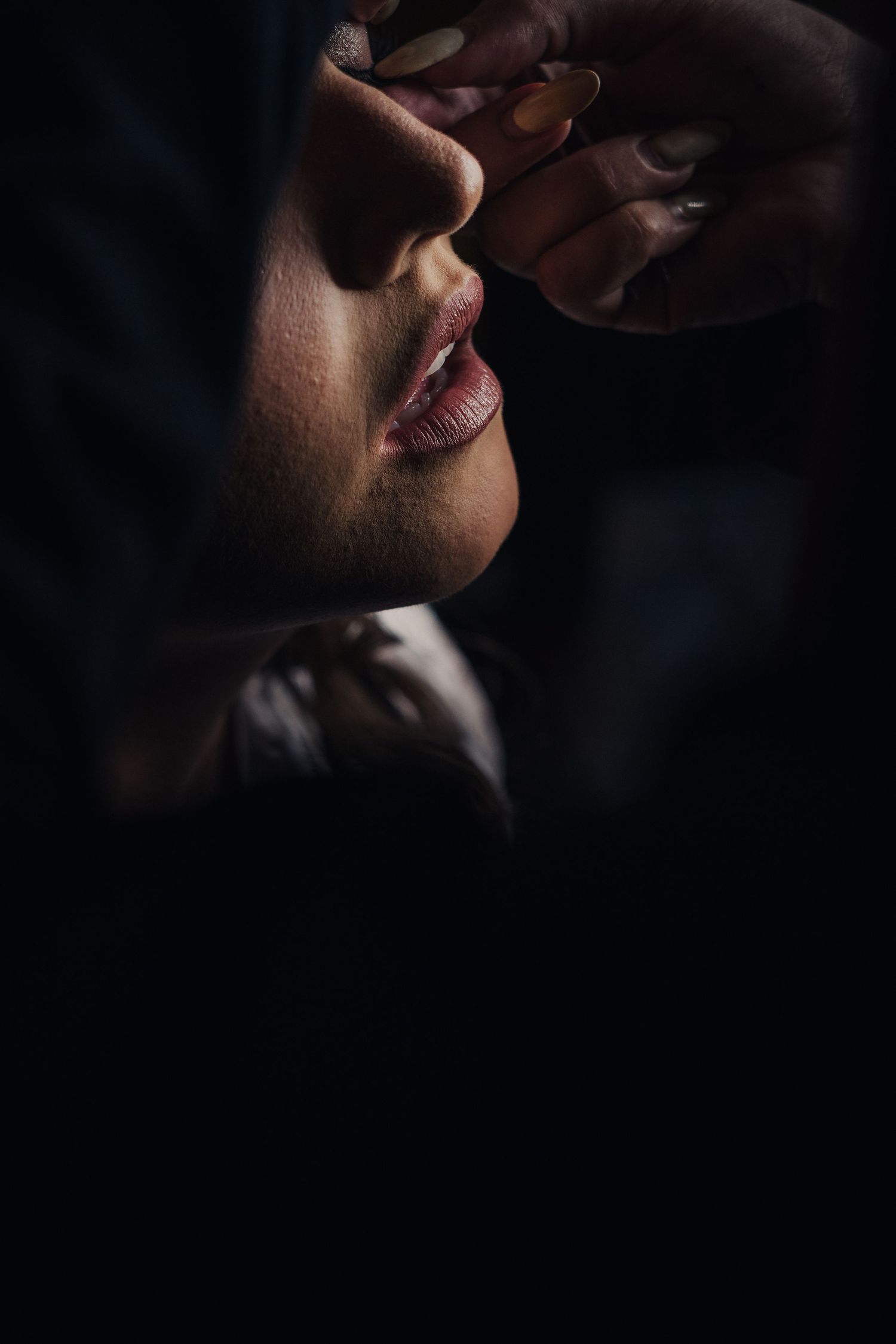 A dramatic close-up portrait in dark lighting shows lips and partial face in shadow.