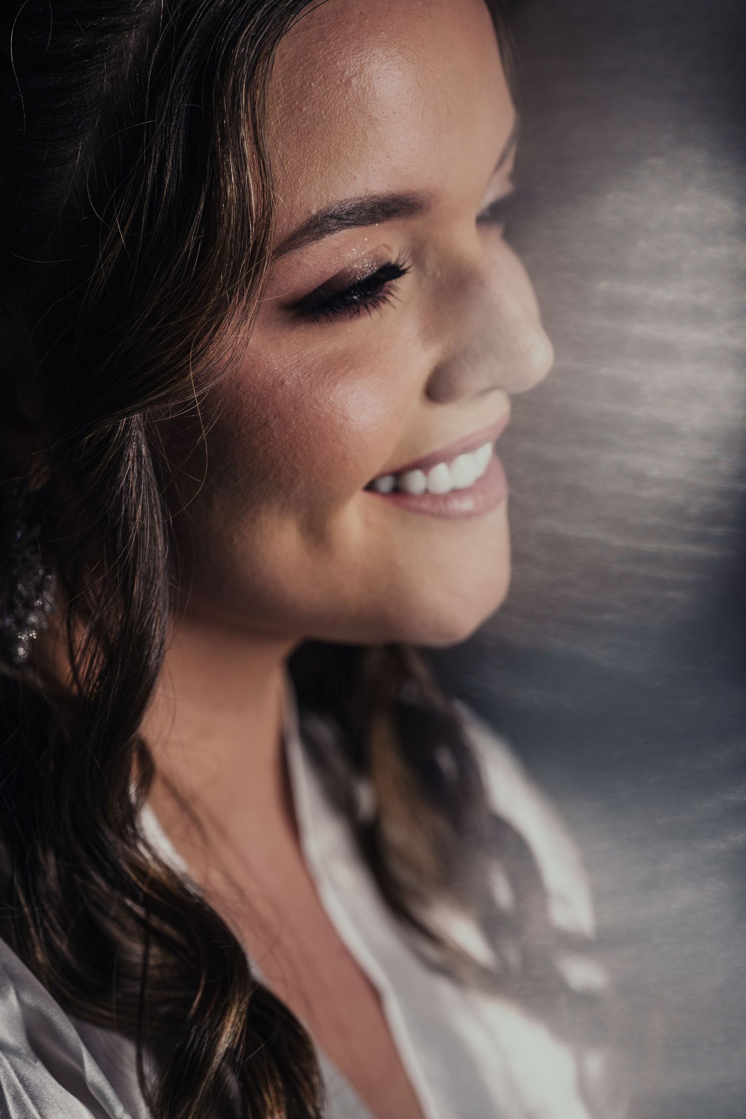 Bride wearing glamorous makeup and long dark hair styled in soft waves with a dreamy, ethereal backdrop.