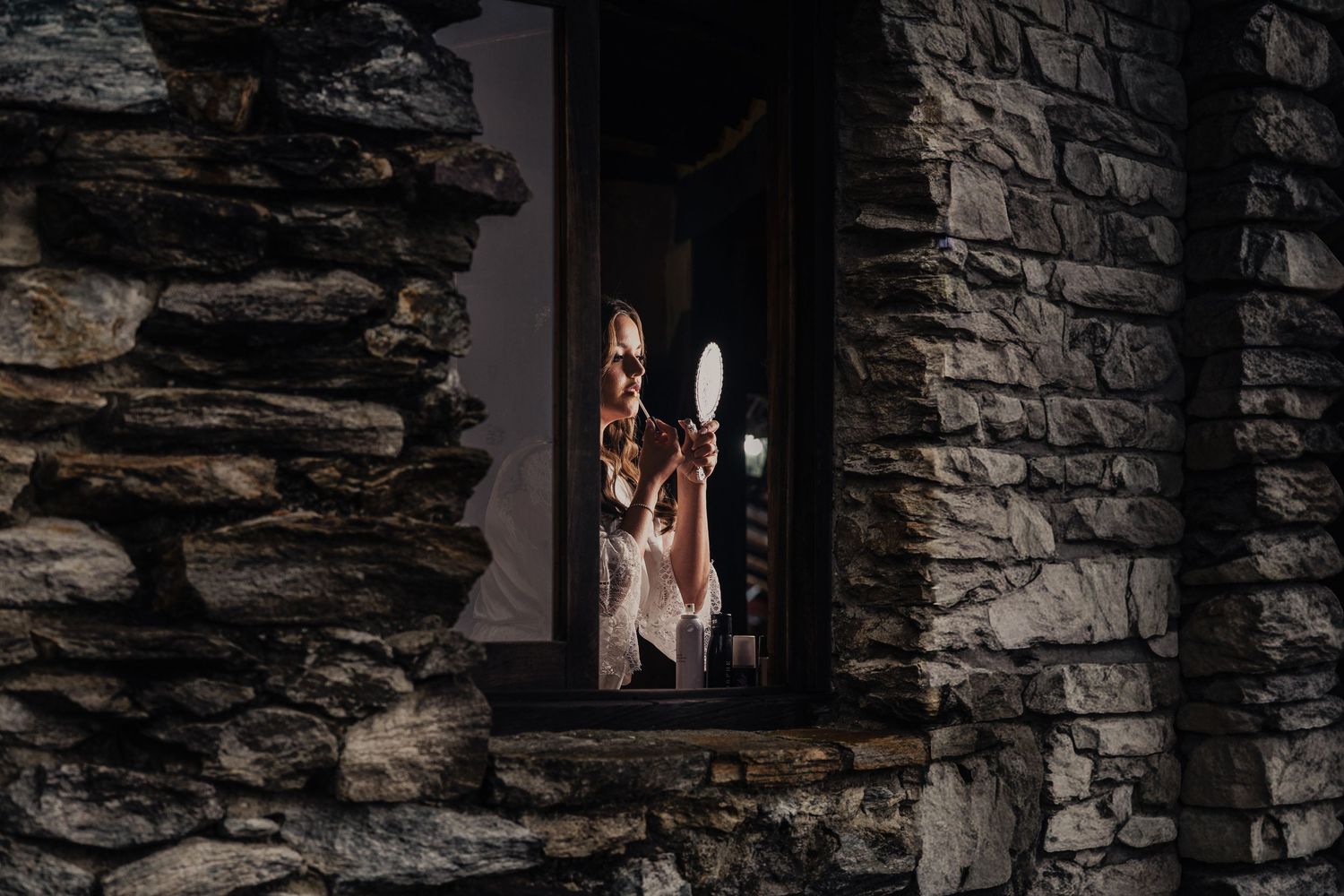 A ghostly figure appears in a dimly lit window of an old stone building at night.
