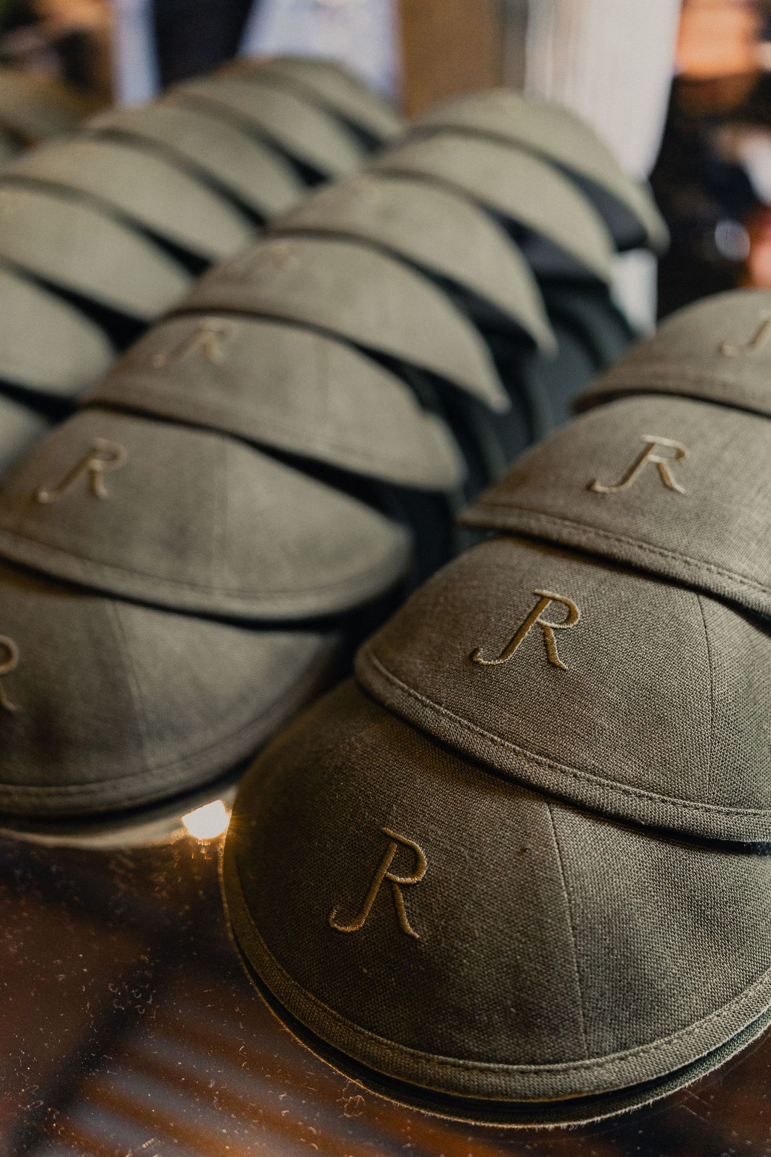 Close-up view of dark gray flat caps with embroidered 'R' monogram detail arranged in a row.