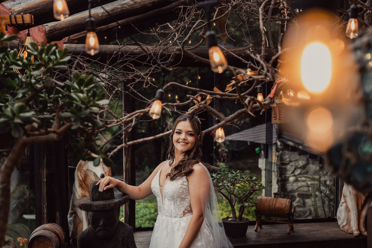 String lights illuminate a rustic outdoor wedding reception venue with wooden beams and natural decor at dusk.